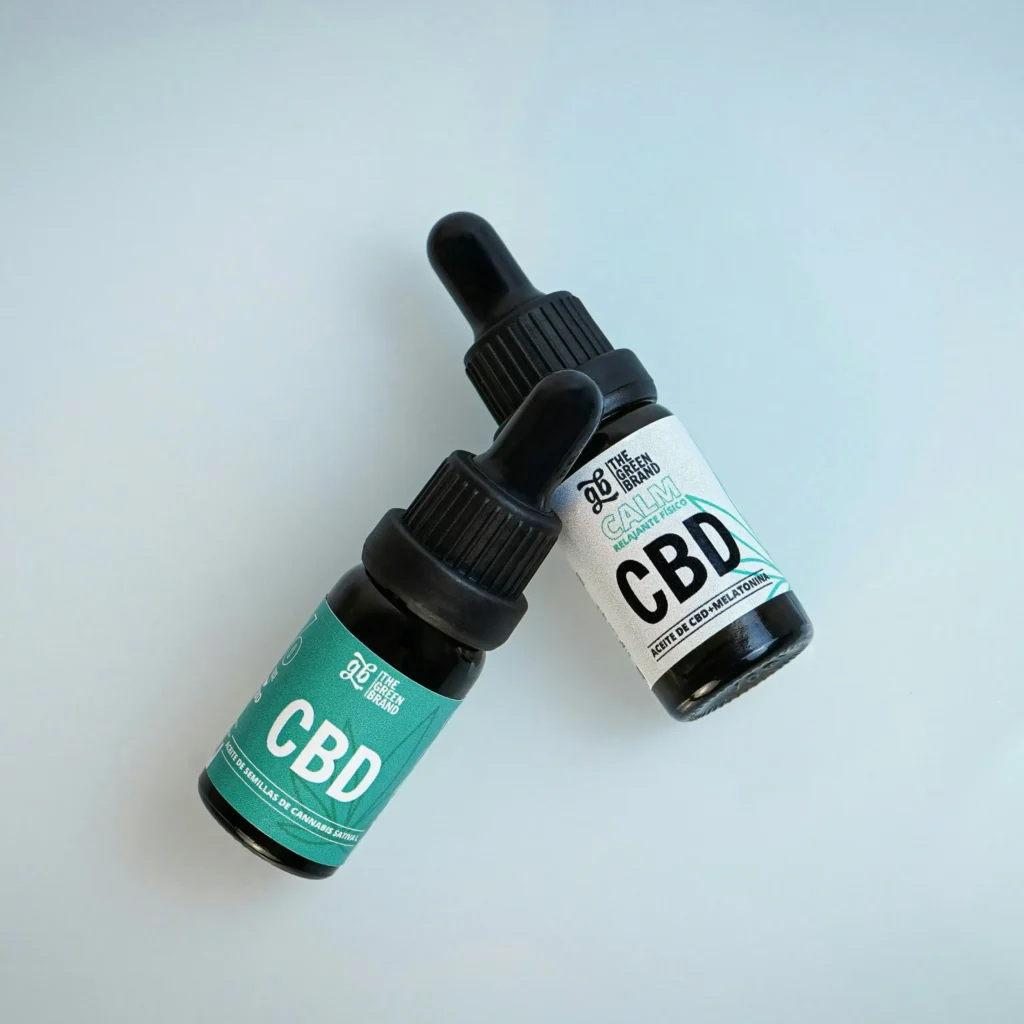 Two dark glass bottles of CBD oil labeled "The Green Brand" with dropper caps, placed on a light surface.